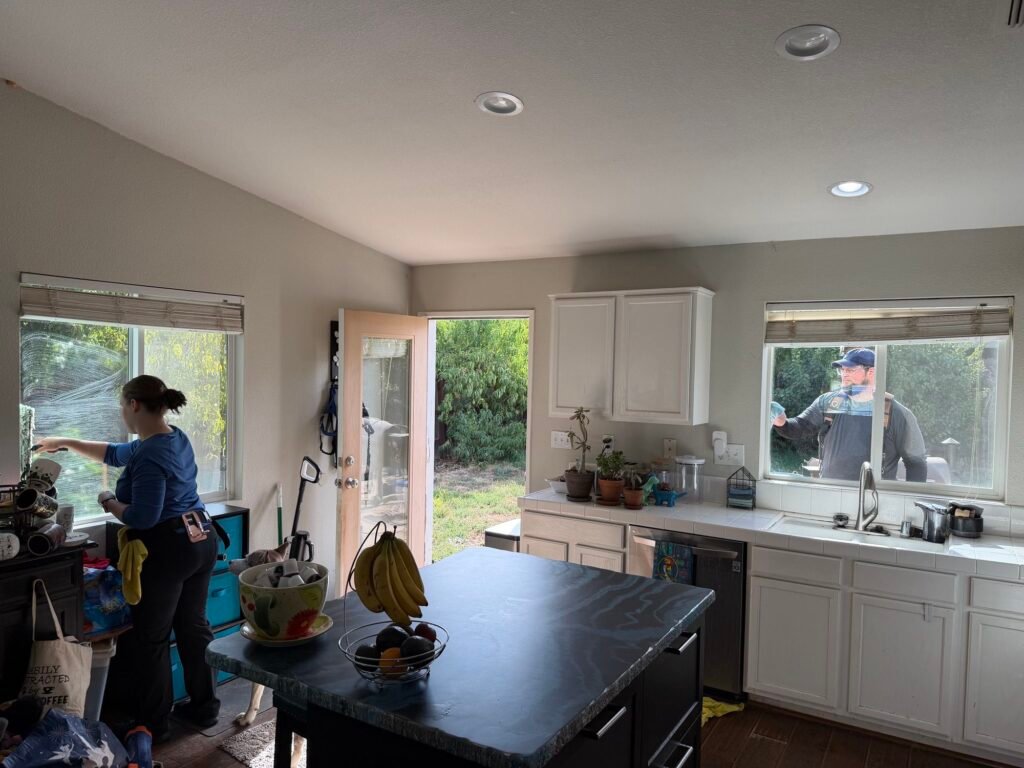 Molly cleaning the inside of a kitchen window while Alex cleans the outside of the same window at a home in Rancho Cordova, CA